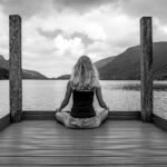 A woman sitting on a dock in front of a body of water