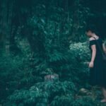 Woman walking through a dark, lush forest.