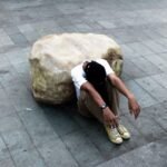 person looking down while siting on concrete pathway during daytime