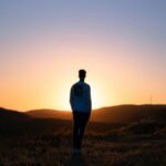 man in blue shirt standing on brown field during sunset